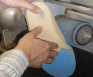 Hands shaping and smoothing a blue and beige piece on a pottery wheel.