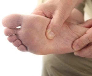 Person pressing a painful spot on the sole of their foot.
